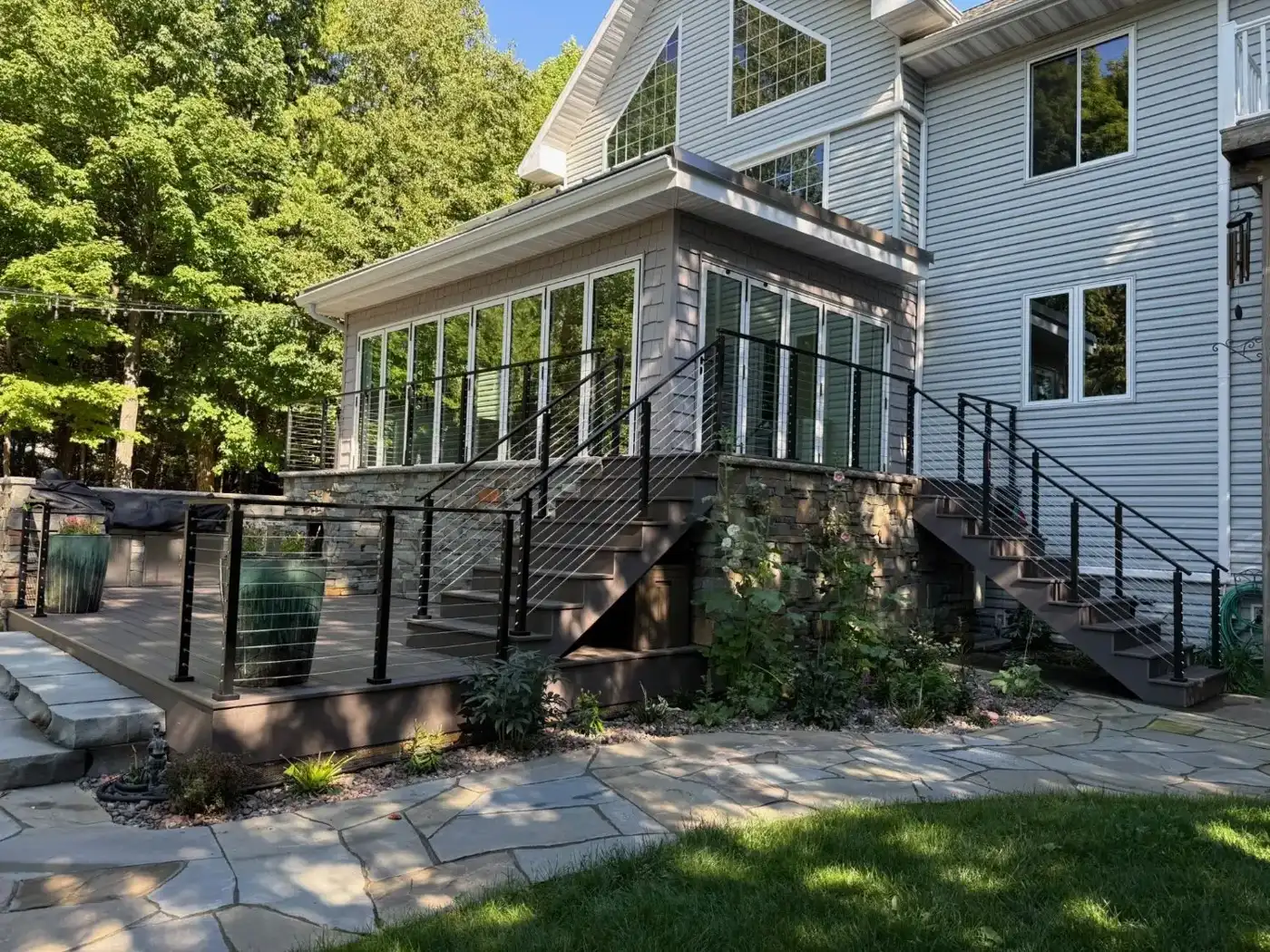 Composite deck with black cable railings and two staircases beside a stone-faced sunroom