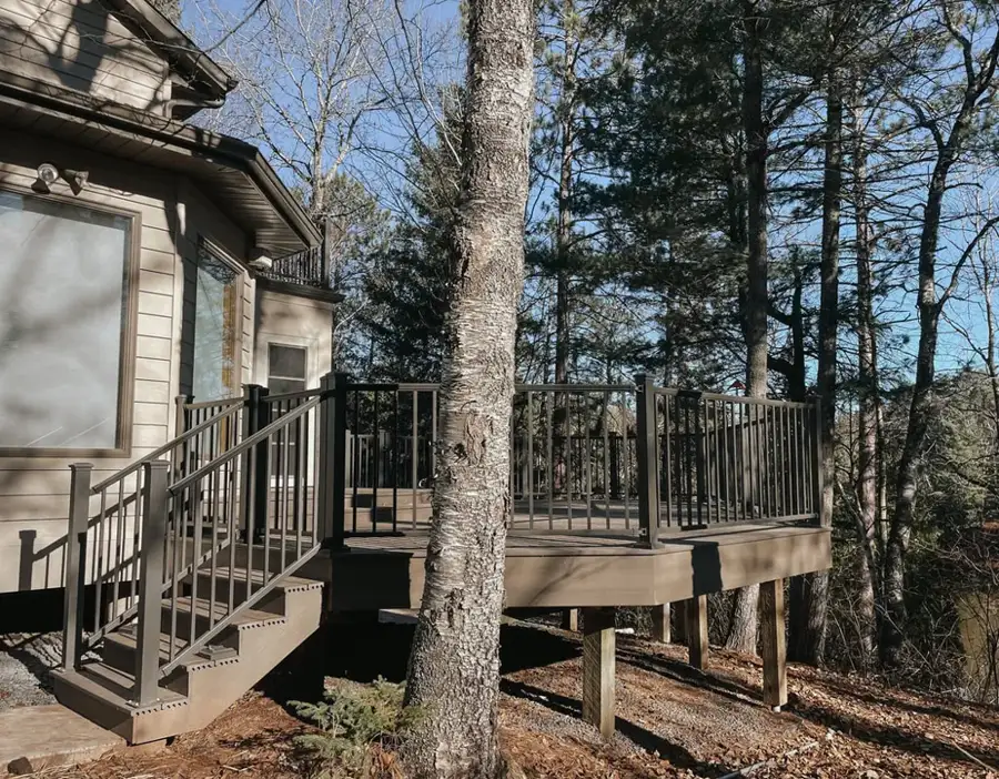 Two-level deck with dark metal railings wrapping a wooded home