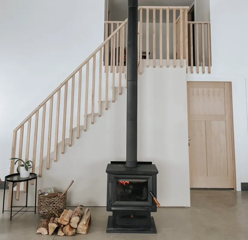 Open staircase with natural wood balusters next to a wood stove