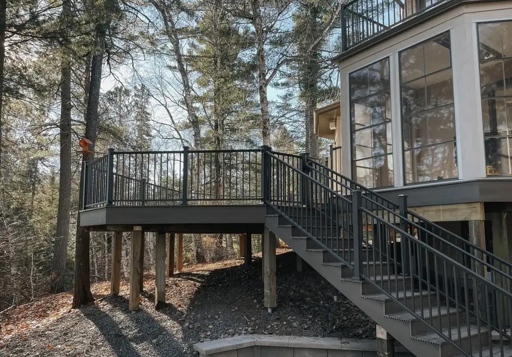 Elevated deck with aluminum railing and stairs among tall pines