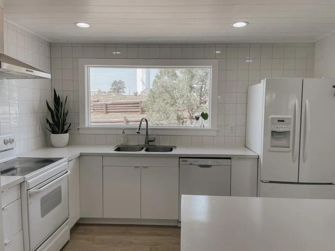 Kitchen with white shaker cabinets, white appliances and a window over the sink